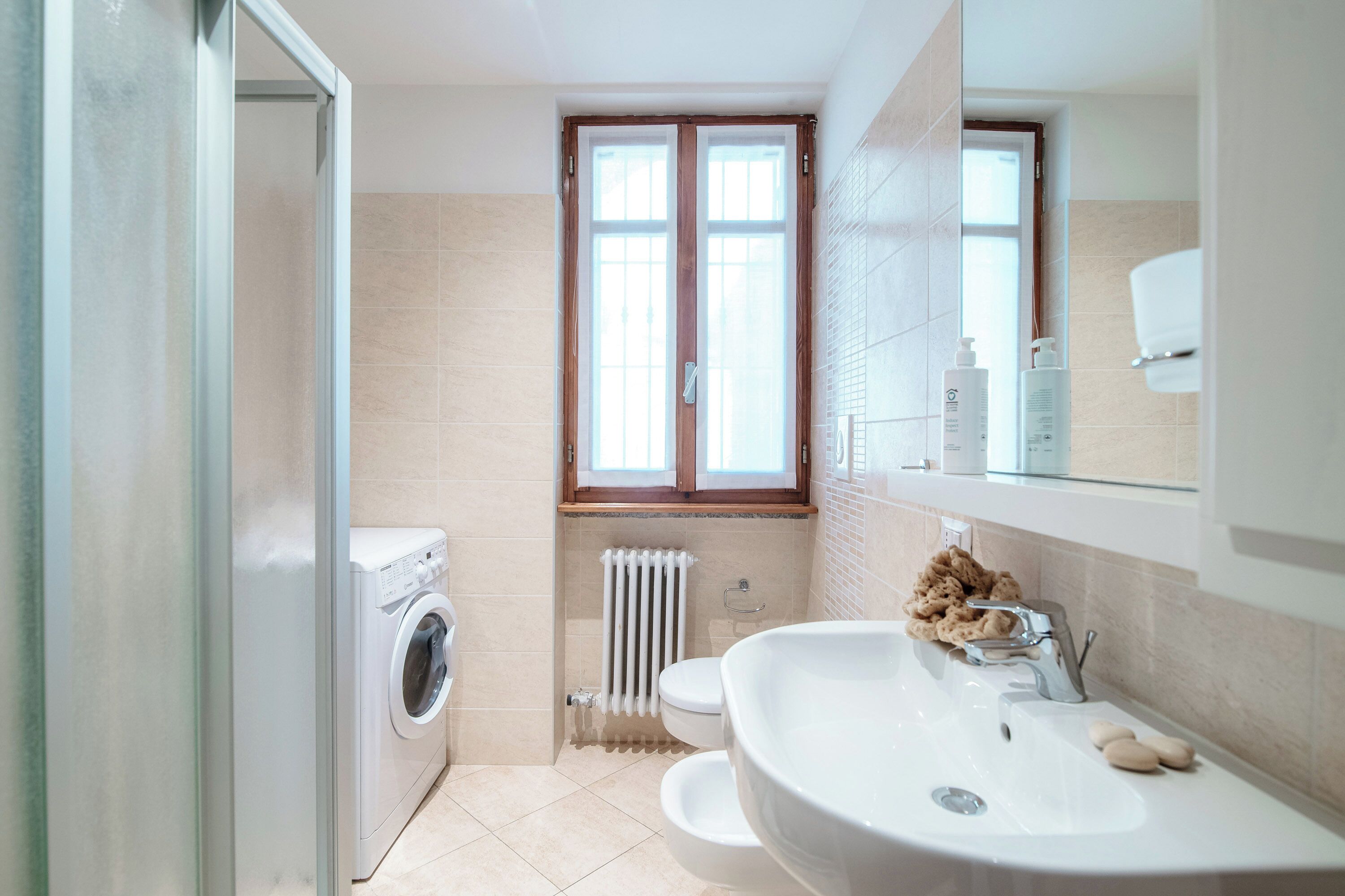 Et moderne badeværelse med en indbygget vaskemaskine, toilet, håndvask og et vindue over toilettet.
