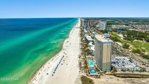 Luftaufnahme eines Küstenresorts mit Strand, einem großen Hotel und einem Parkplatz.