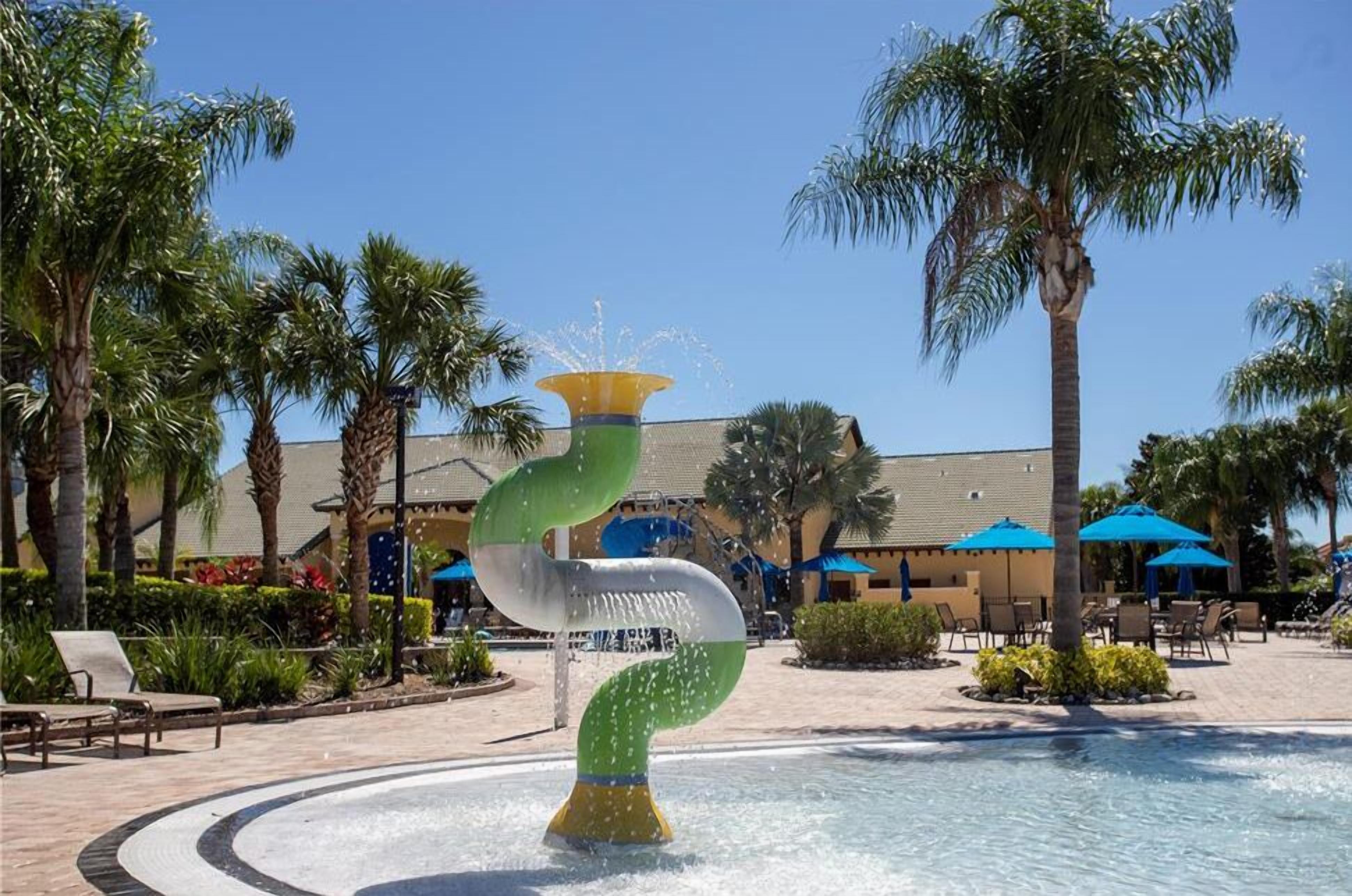 A water feature with a spiral design, surrounded by palm trees and lounge chairs, with a building in the background.