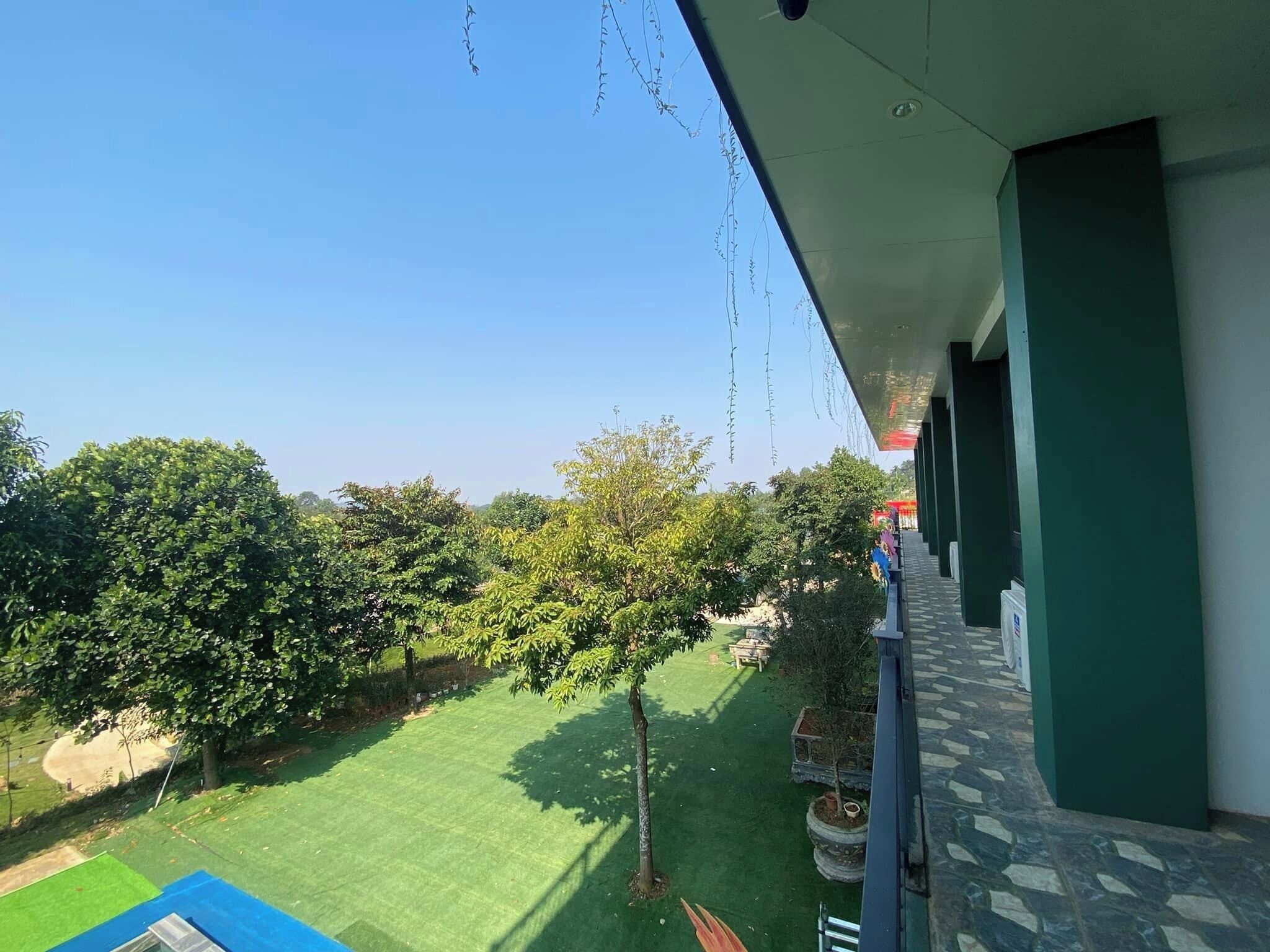 A balcony with a clear view of a green lawn and trees.
