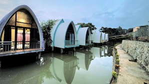 Een rij moderne, gebogen gebouwen op waterpeil met balkons, weerspiegeld in het wateroppervlak.