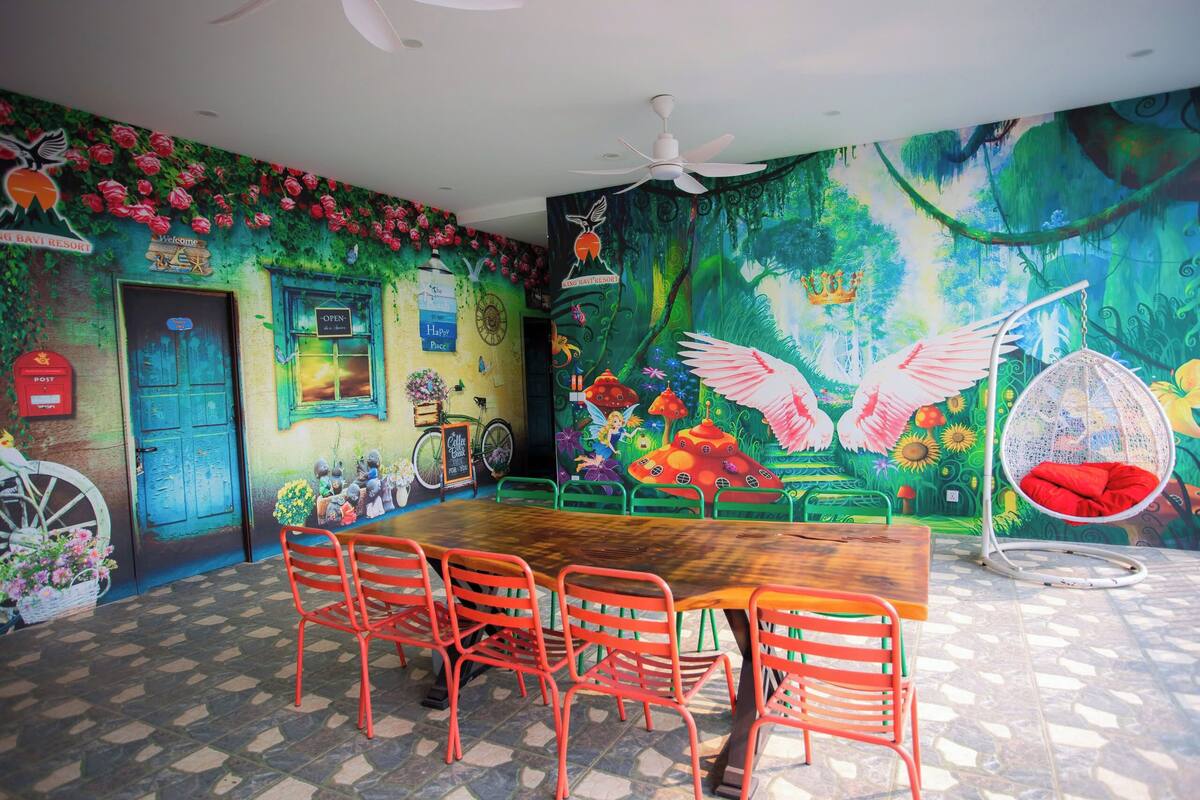 Un comedor con una mesa de madera y sillas rojas, un mural con pájaros y flores, y una silla colgante con un cojín rojo.