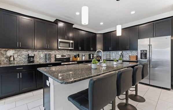 A modern kitchen with dark cabinets, stainless steel appliances, a granite countertop, and a central island with bar stools.