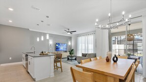 Et moderne køkken med en central ø, et spiseområde med et træbord og stole, en stue med sofa og TV, samt en balkon med udsigt.