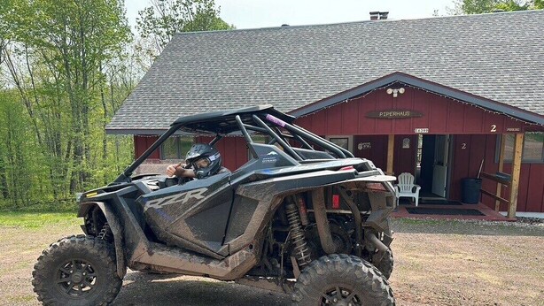 Een Polaris RZR offroad voertuig geparkeerd voor een rustiek gebouw met een bord waarop 'Piperhaus' staat.