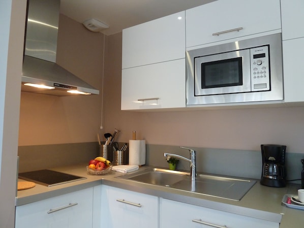A modern kitchen with white cabinets, a stainless steel microwave, a sink, and a coffee maker.