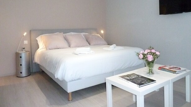 Ein modernes Schlafzimmer mit Bett, Nachttisch und einem am Wand montierten Fernseher.