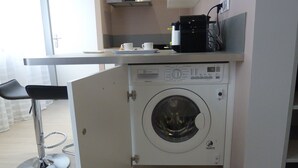 Eine kleine Küche mit integrierter Waschmaschine und Trockner, einer kompakten Arbeitsfläche und einem Barhocker.