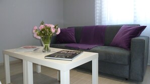 Ein modernes Wohnzimmer mit einem grauen Sofa, einem weißen Couchtisch und einer Vase mit rosafarbenen Blumen.