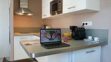 A compact kitchen with a microwave, coffee maker, and a laptop on the counter.