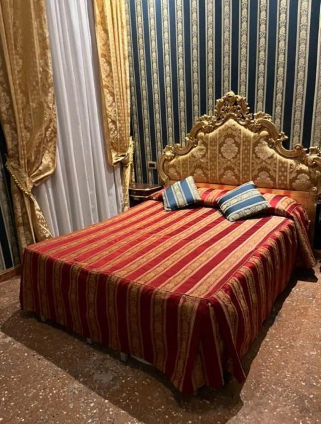 Una cama con una colcha a rayas doradas y rojas, un cabecero dorado y dos almohadas.