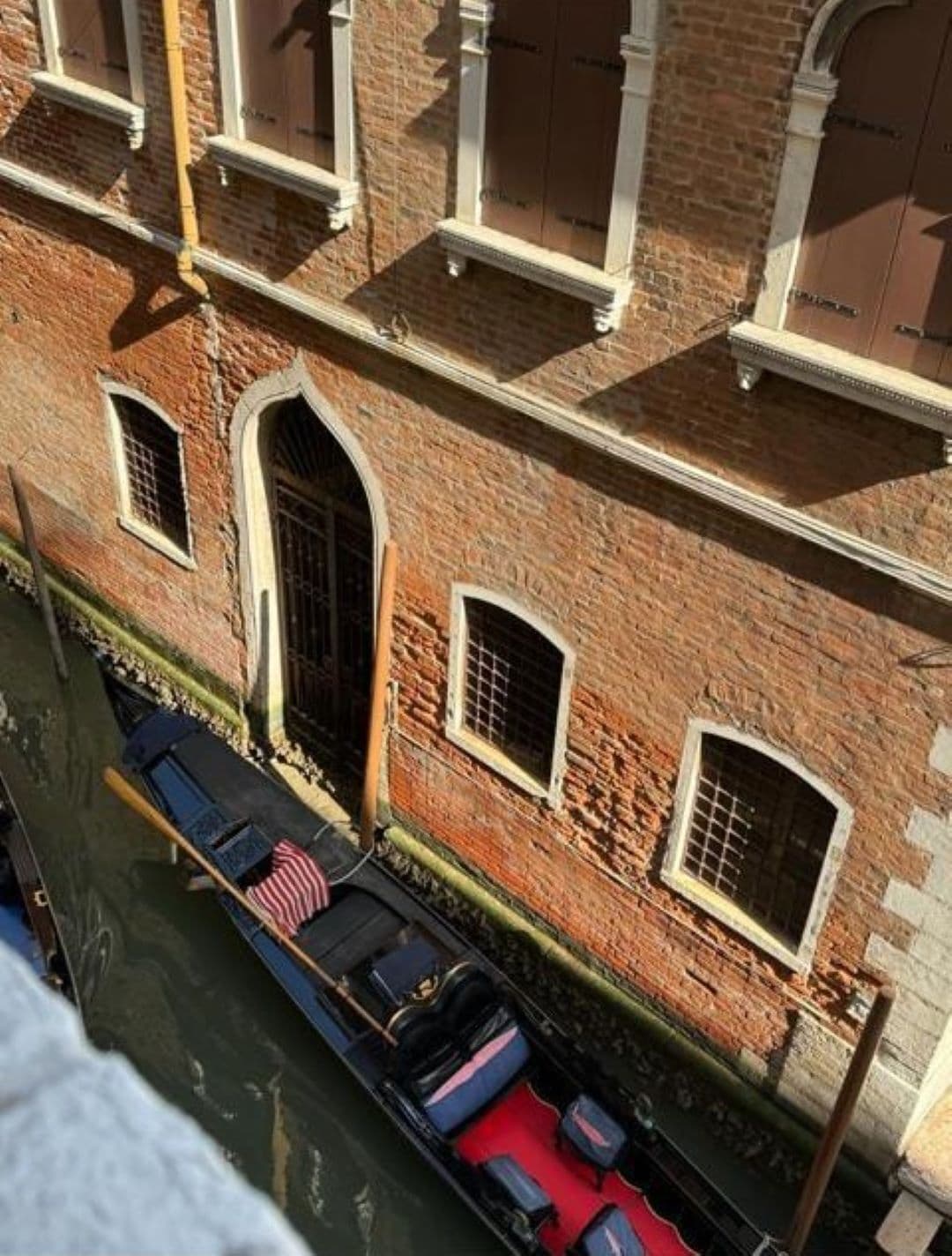 Un edificio junto a un canal, con varios ventanales y una embarcación atracada frente a él.