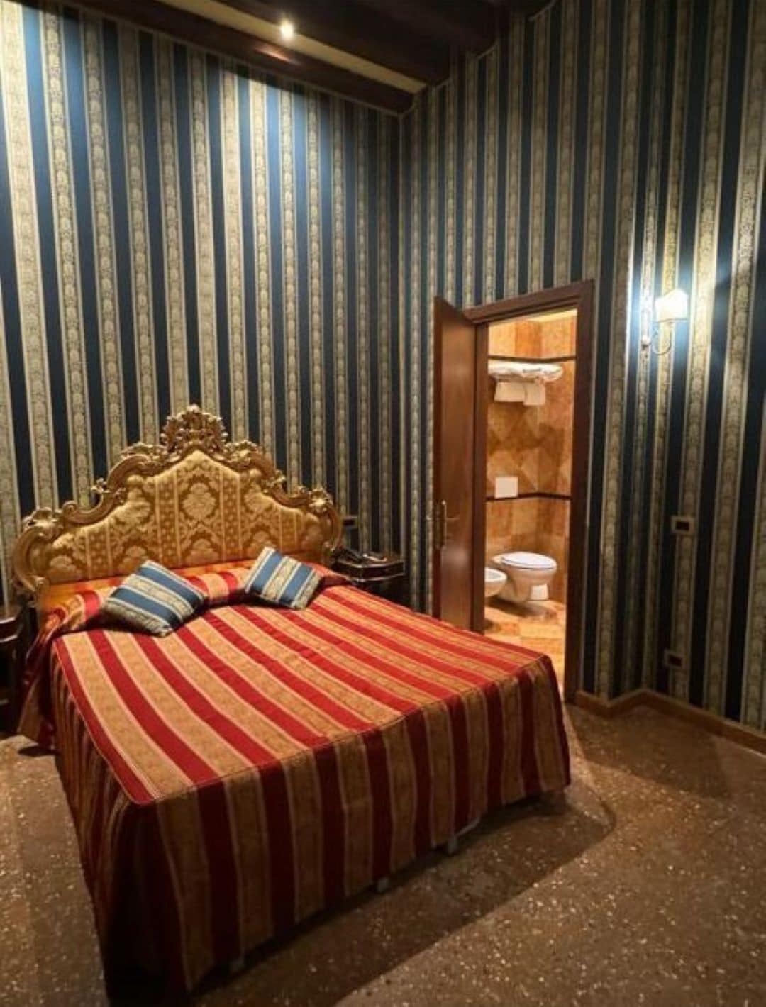 A bedroom with a large bed, striped bedding, a wooden headboard, and a bathroom visible through an open door.