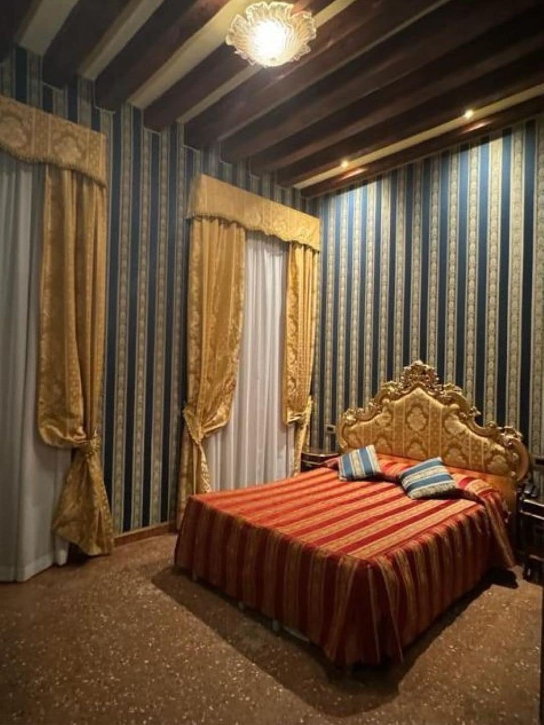 A room with a large bed, striped wallpaper, and curtains.