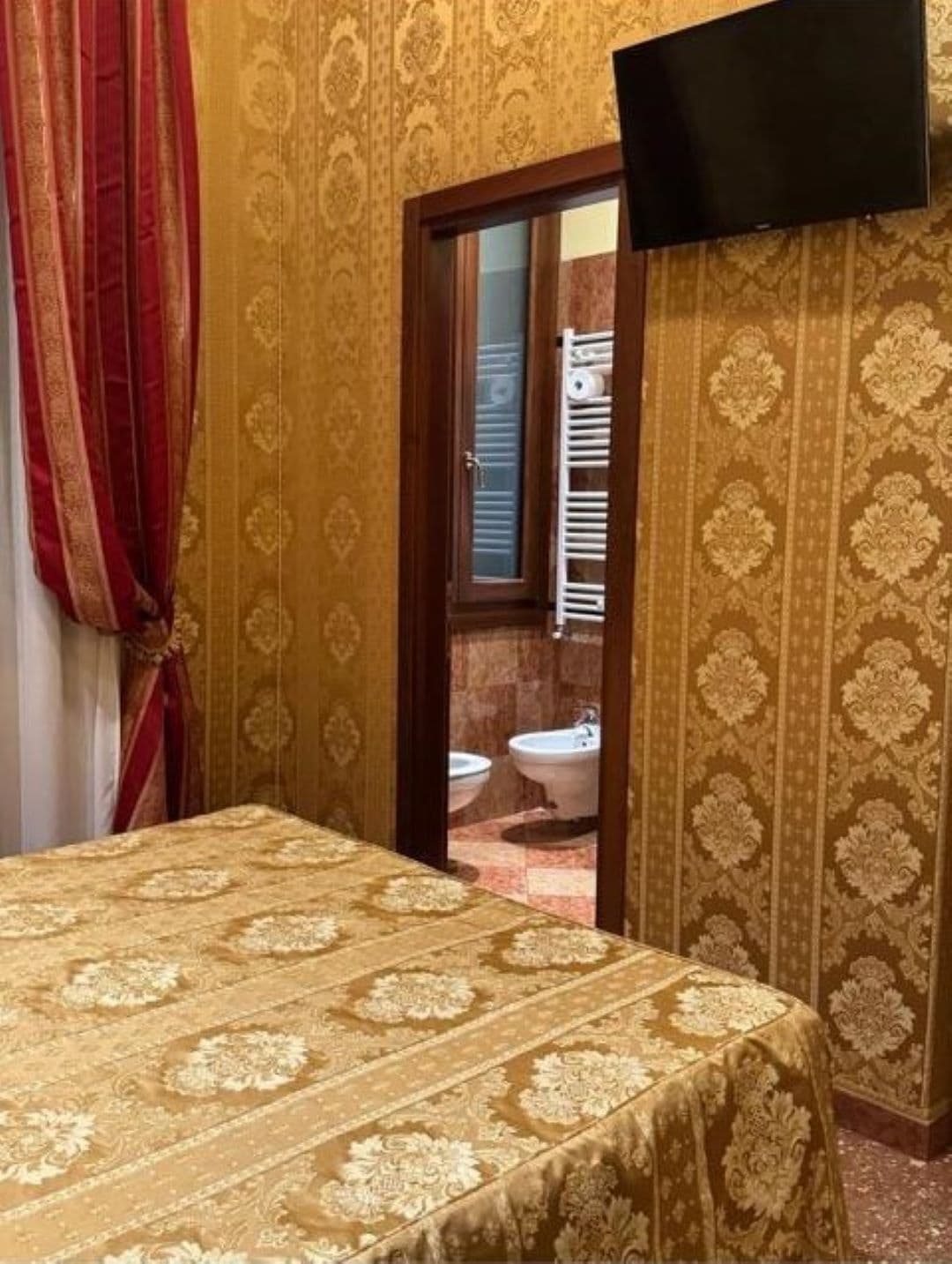 A hotel room with a bed, a television mounted on the wall, and a view of the bathroom through an open door.