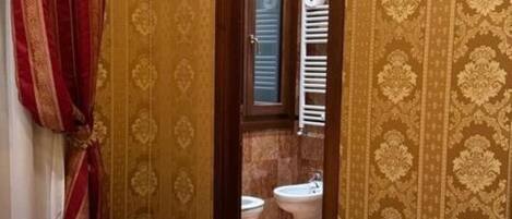 A hotel room with a bed, a television mounted on the wall, and a view of the bathroom through an open door.