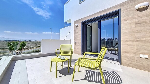 Een modern balkon met twee gele stoelen en een kleine tafel, grote schuifdeuren en uitzicht op het landschap.