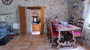 Une salle à manger aux murs de pierre, avec une table dressée pour six personnes, des chaises en bois et une vue sur la cuisine.