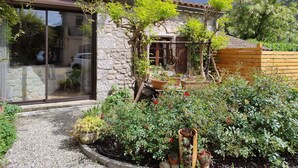 Un bâtiment en pierre doté d’un jardin agrémenté de plantes en pot et d’une clôture en bois.