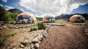 Tre geodætkupler i et naturligt landskab med et bjergrigt baggrund.