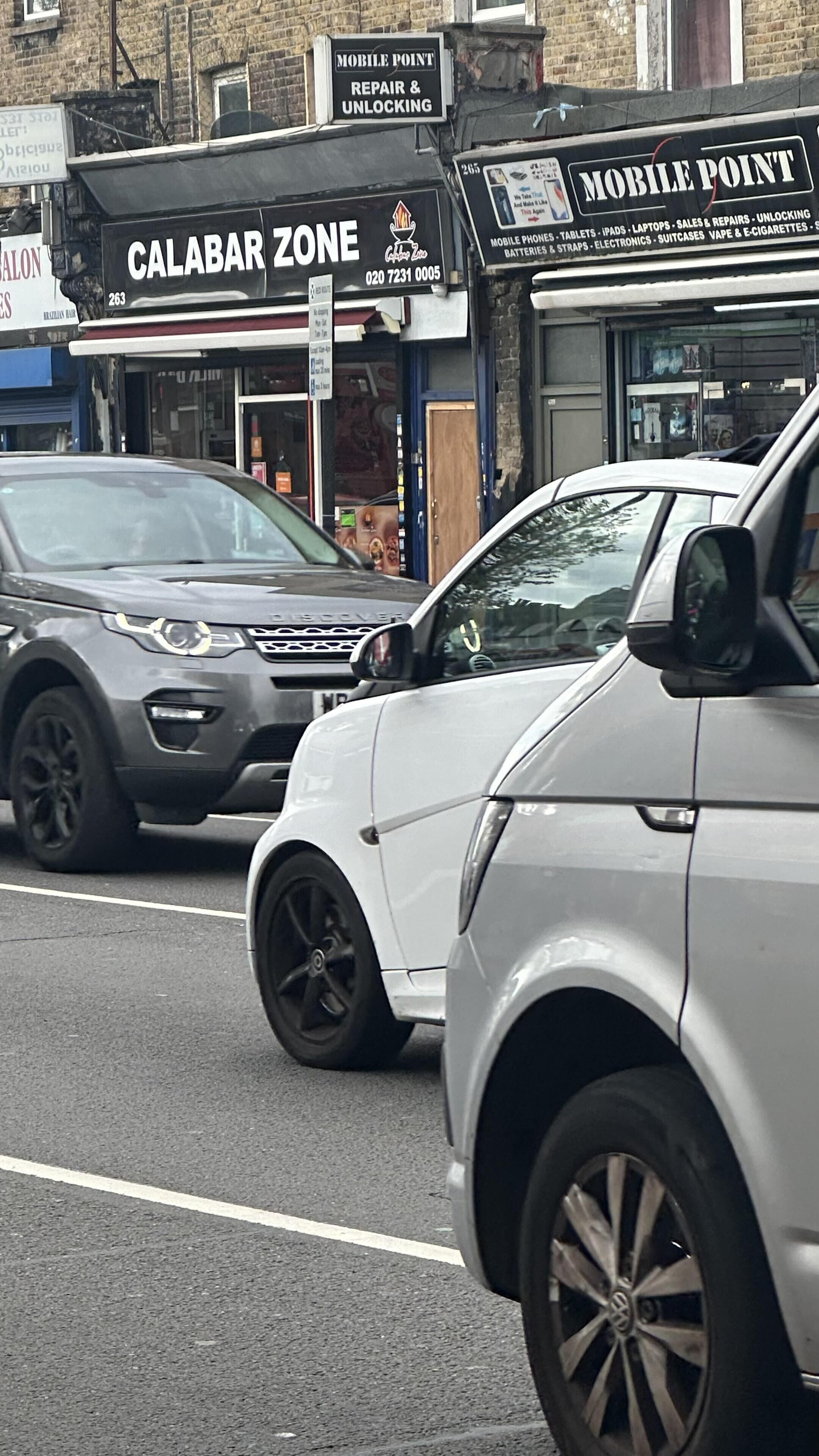A street view with a white SUV parked in front of a building with signs for 'CALABAR ZONE' and 'MOBILE POINT'.