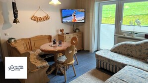 Een knus ingerichte kamer met een houten eettafel, een bank en een aan de muur bevestigde televisie.