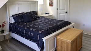 Een slaapkamer met een bed, nachtkastje, lamp en een deur.