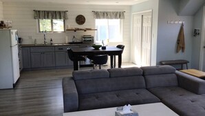 Een moderne keuken met witte kasten, een eethoek met een donker houten tafel en stoelen, en een grijze bank in de woonkamer.