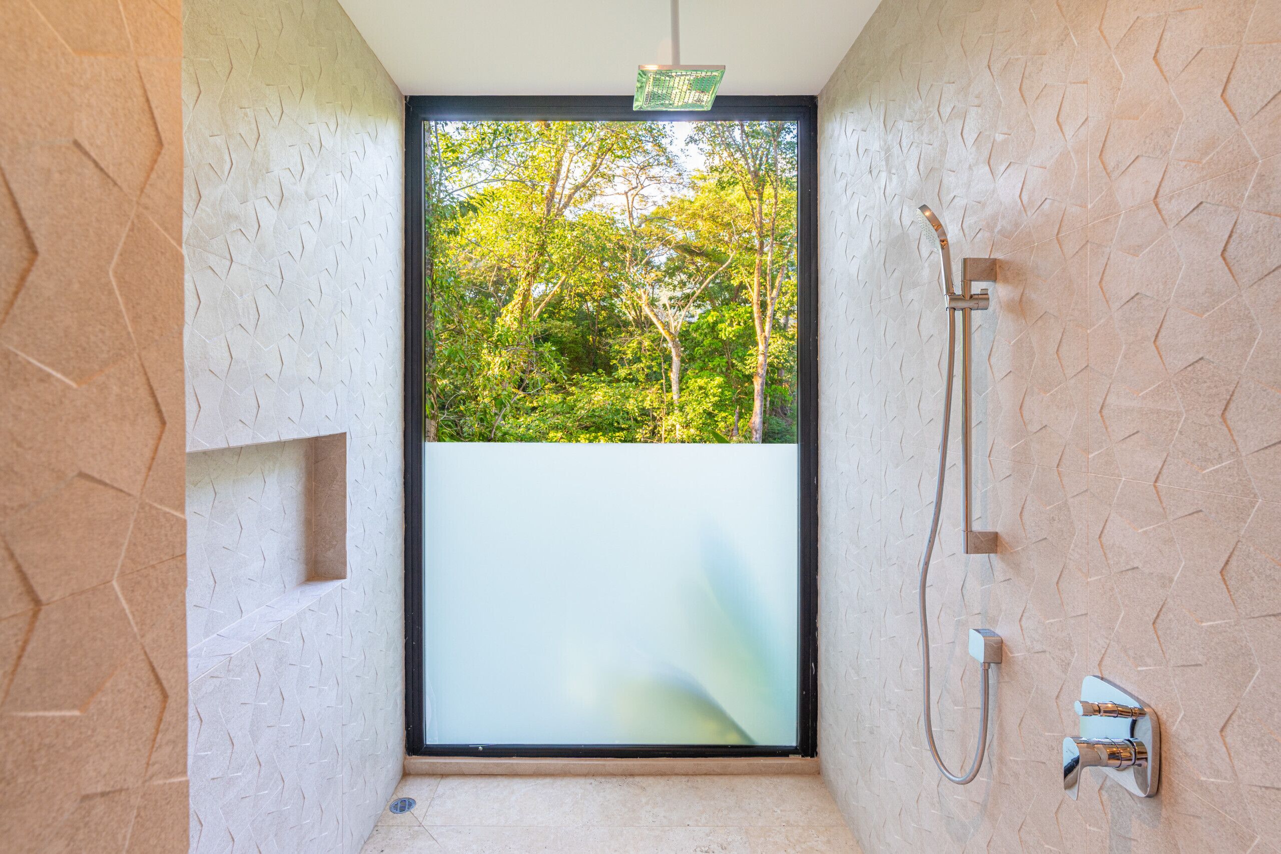 A modern bathroom with a glass door leading to a balcony, a shower area, and a textured wall.