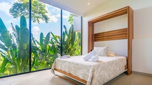 A bedroom with a large window, a bed with a wooden headboard, and a view of lush greenery. - Casa Colibri by Pura Villas (Uvita)