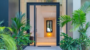A modern building entrance with a glass door, surrounded by lush greenery. - Casa Colibri by Pura Villas (Uvita)