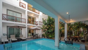 A modern indoor swimming pool with multiple lounge areas, a covered seating area, and a view of the surrounding greenery. - HOTEL CARACOL ISLA MUJERES (Isla Mujeres)