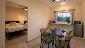 A room with a bed, a dining table with chairs, a ceiling fan, a window with curtains, a microwave, and a small kitchenette. - HOTEL CARACOL ISLA MUJERES (Isla Mujeres)