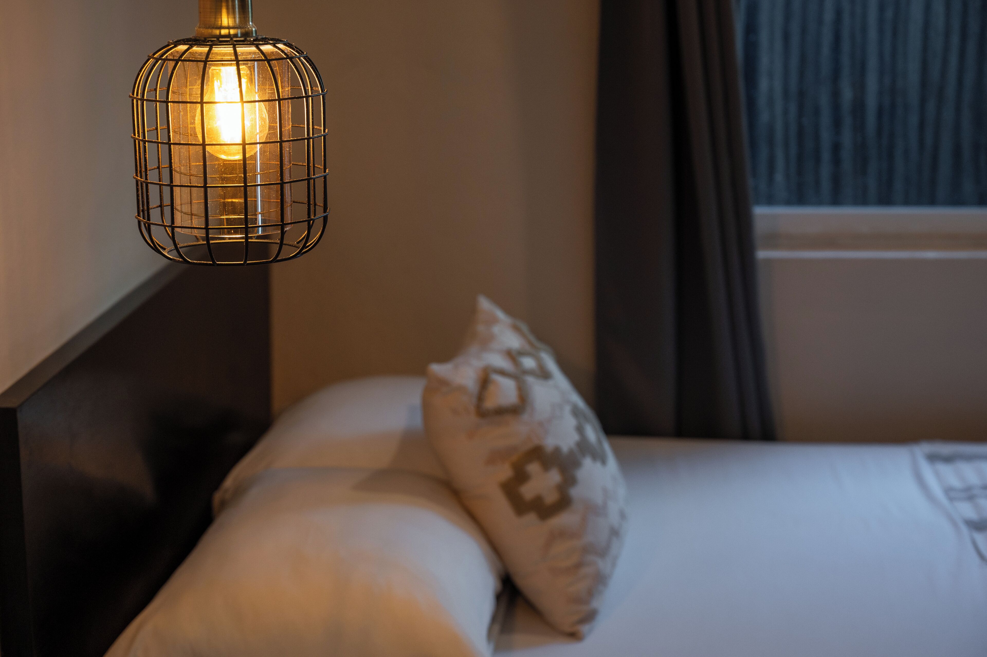 En säng med ett mönstrat kuddöverdrag och en hängande lampa.