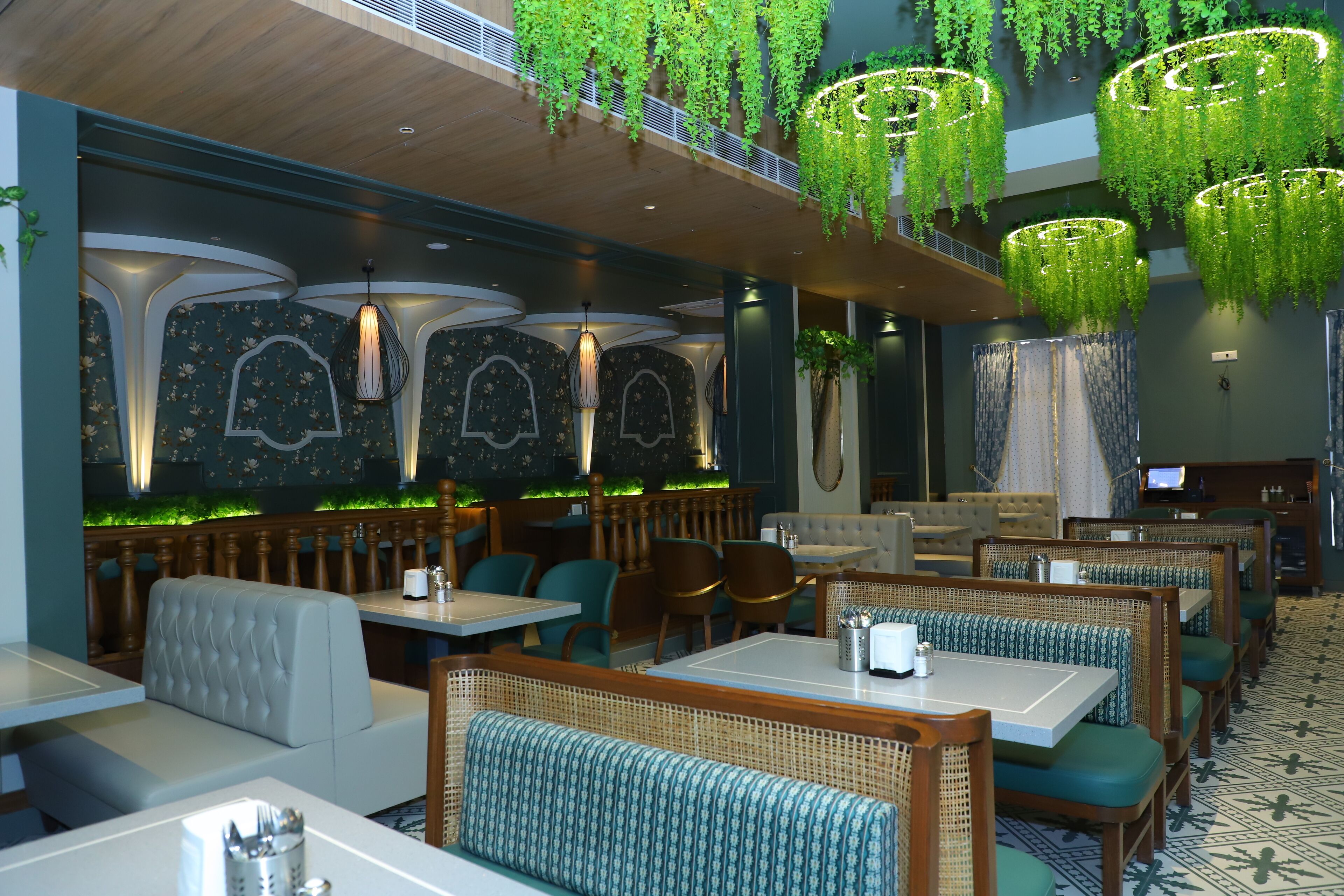 A restaurant with booths and tables, hanging green plants, and patterned walls.