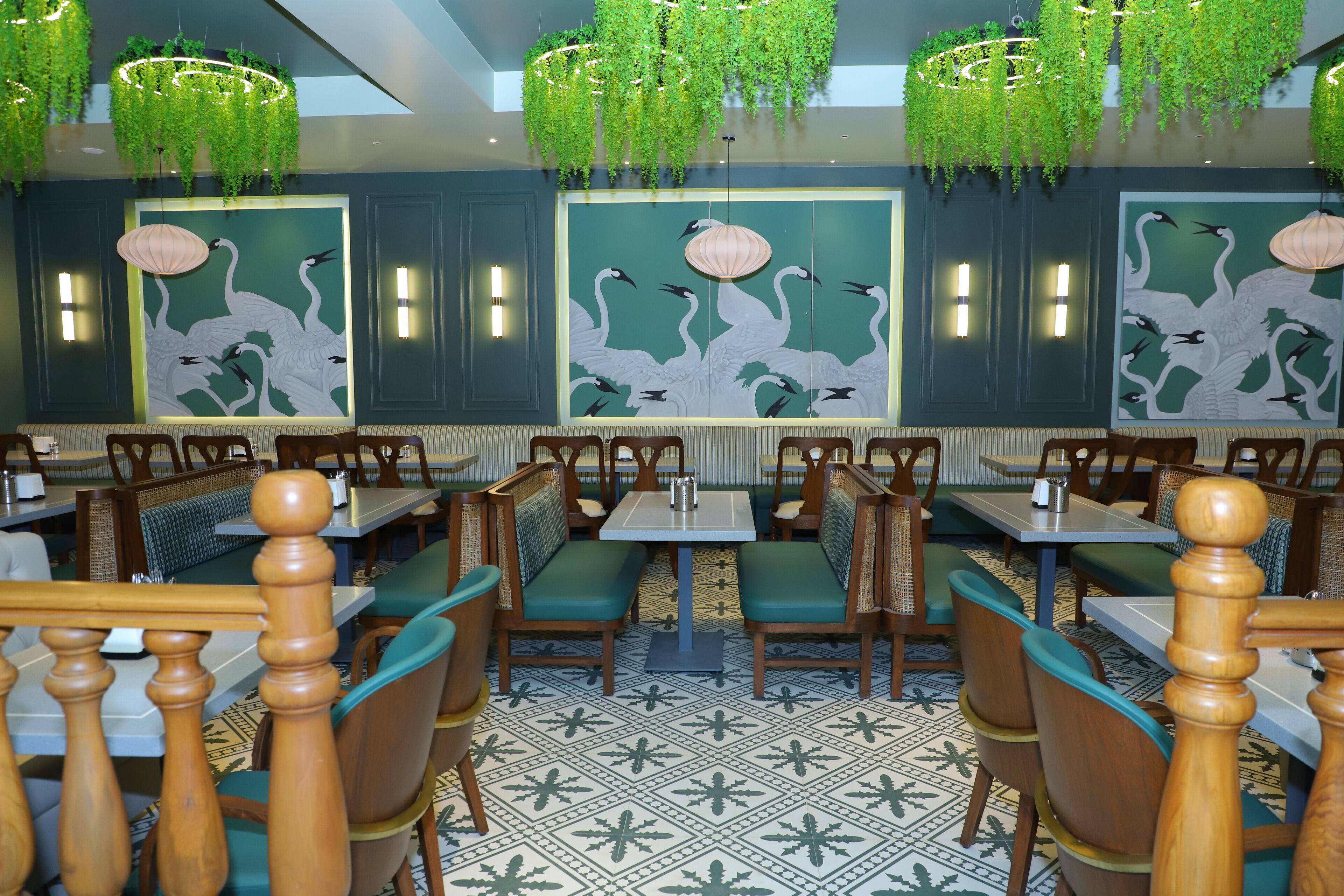 A restaurant with green upholstered booths, patterned floor tiles, and wall art of swans.