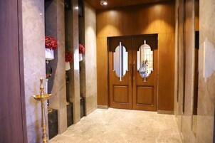 Um corredor com piso de mármore, um abajur de latão tradicional e uma porta de madeira com um espelho.