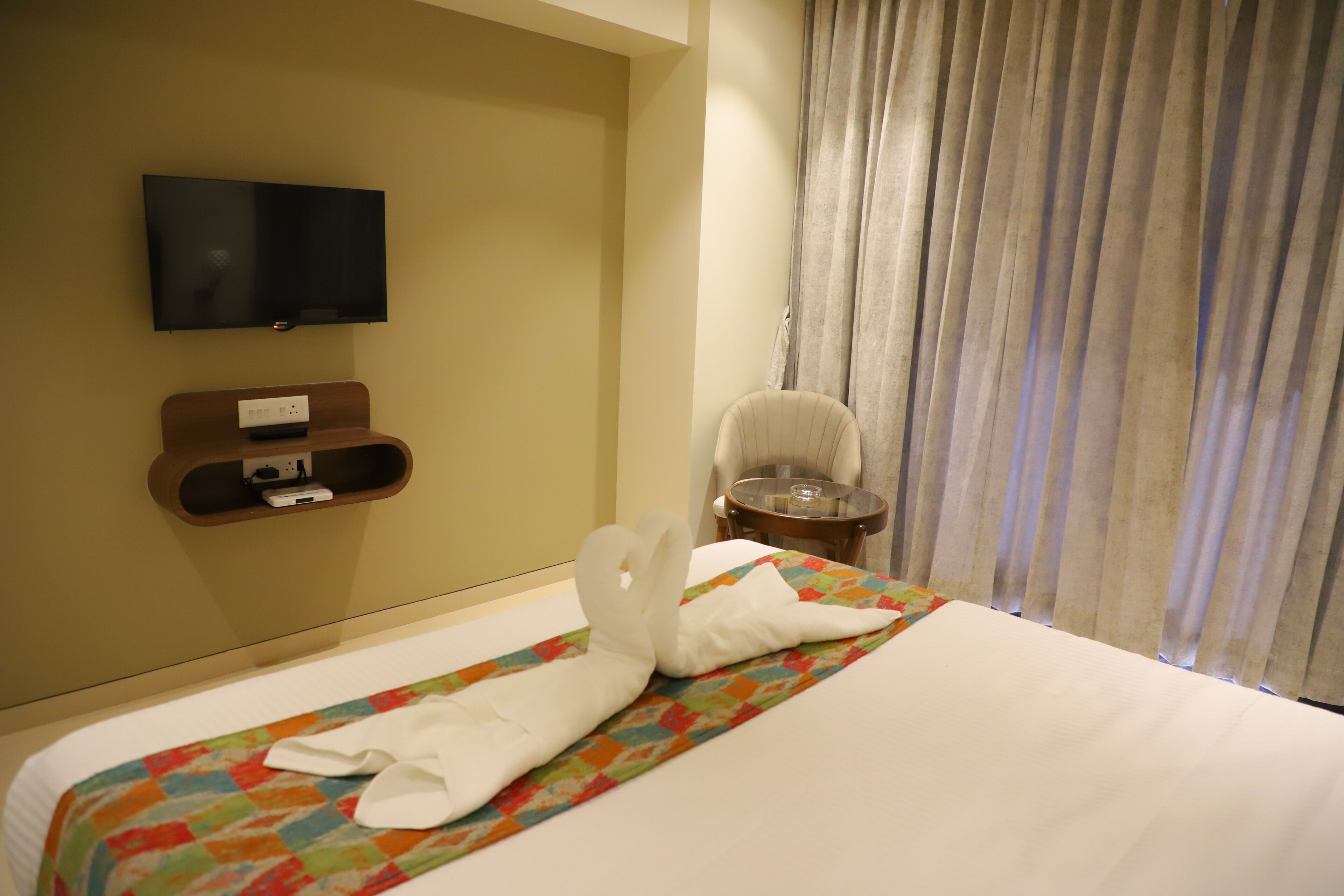 Una habitació d'hotel amb un llit, una televisió penjada a la paret, una taula petita i una cadira.
