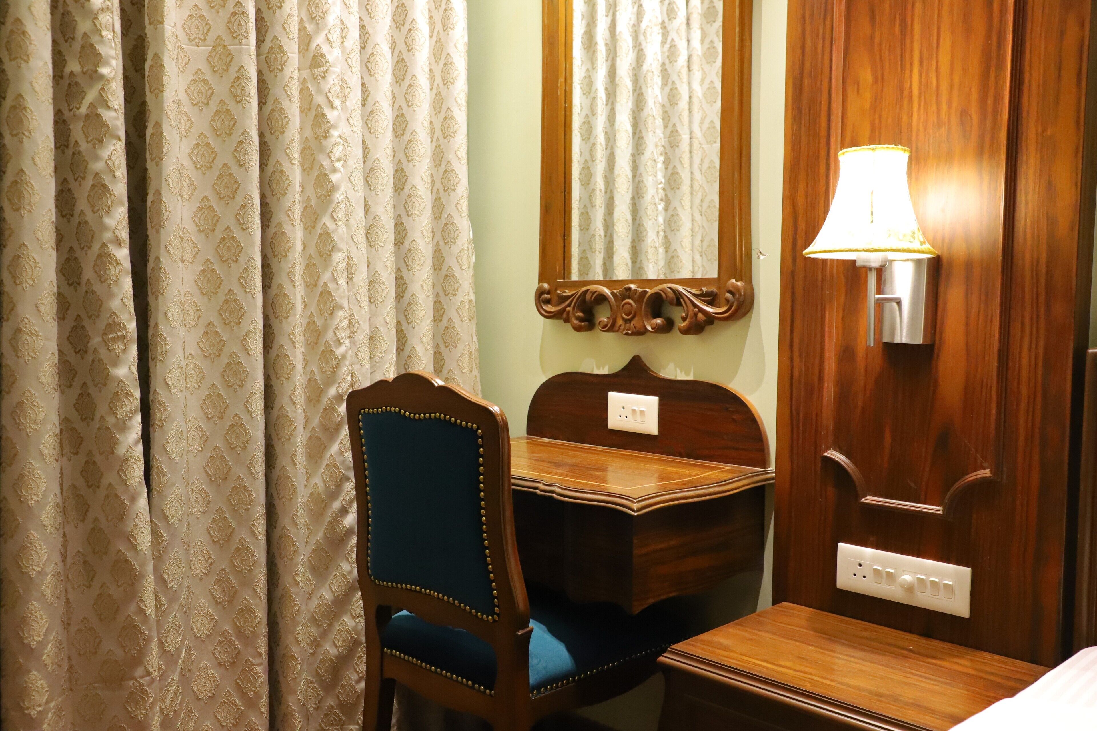 A room with a wooden desk, a chair, a mirror, a lamp, and a bed.