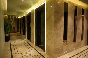 Um corredor com piso de mármore, um vaso de planta e várias portas de elevador.