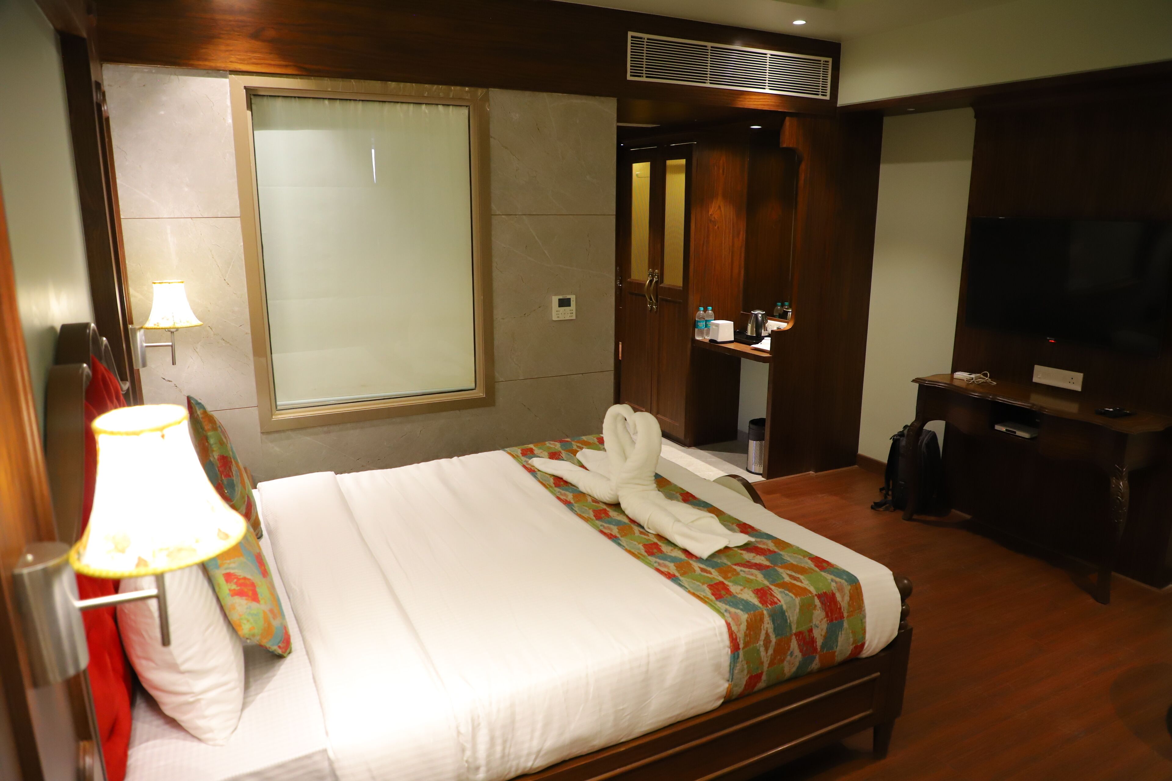 A hotel room with a bed, a TV, a desk, and a mirror.