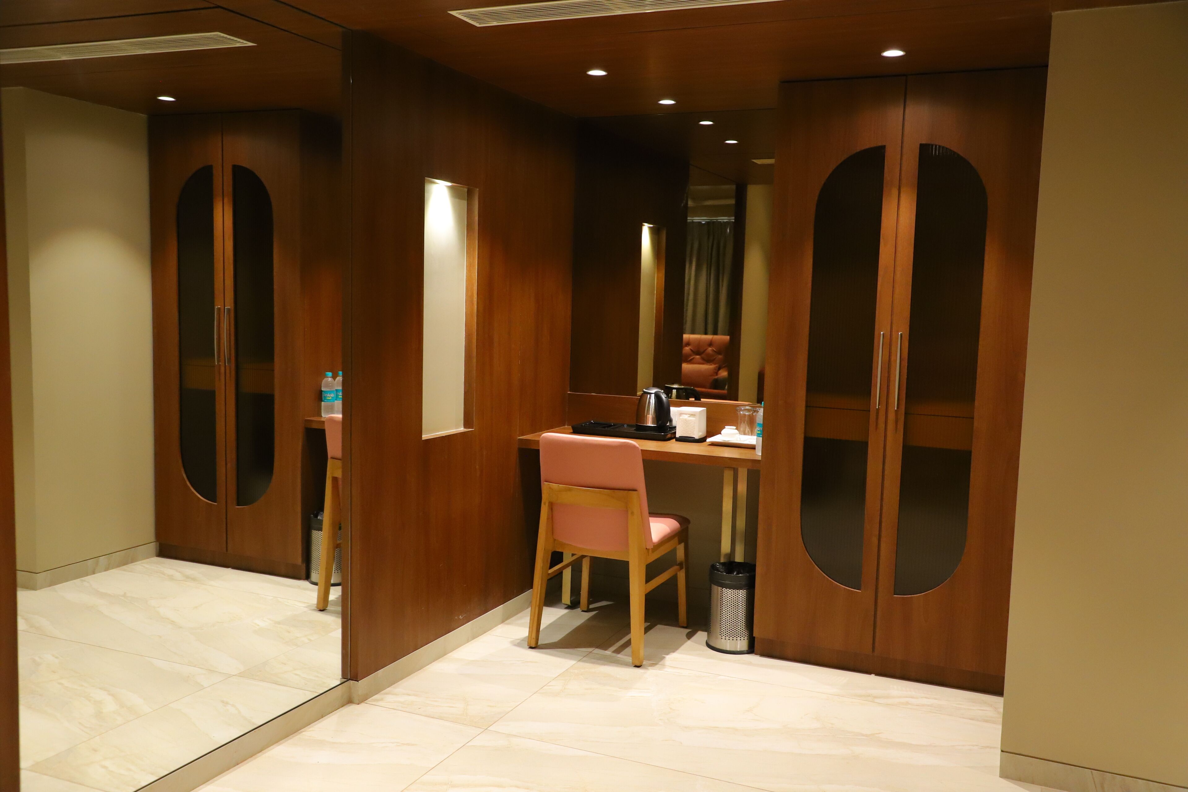 A hotel room with a wooden desk, a chair, a mirror, and a wardrobe with two doors.