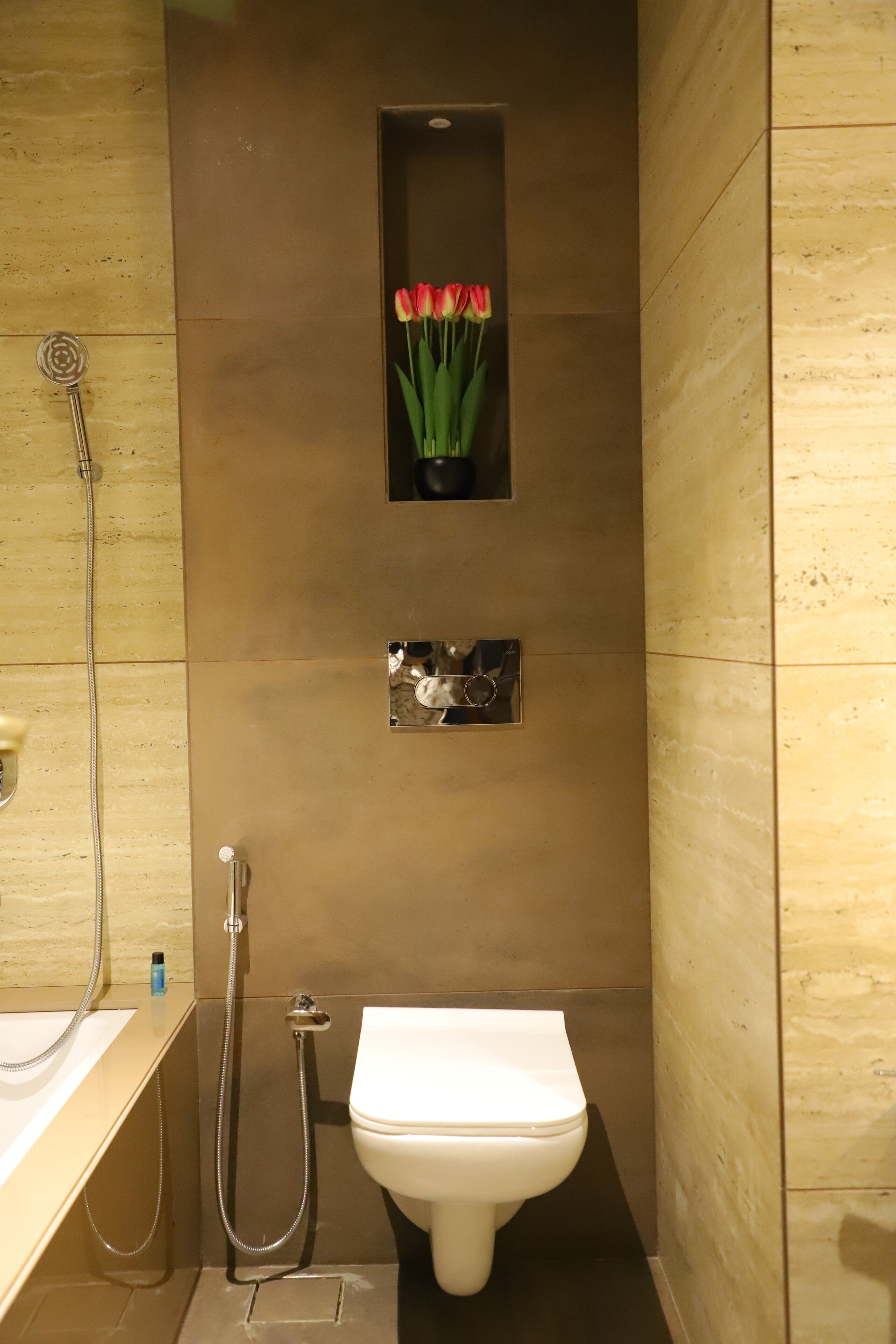 A modern bathroom with a toilet, a shower, and a small shelf with flowers.