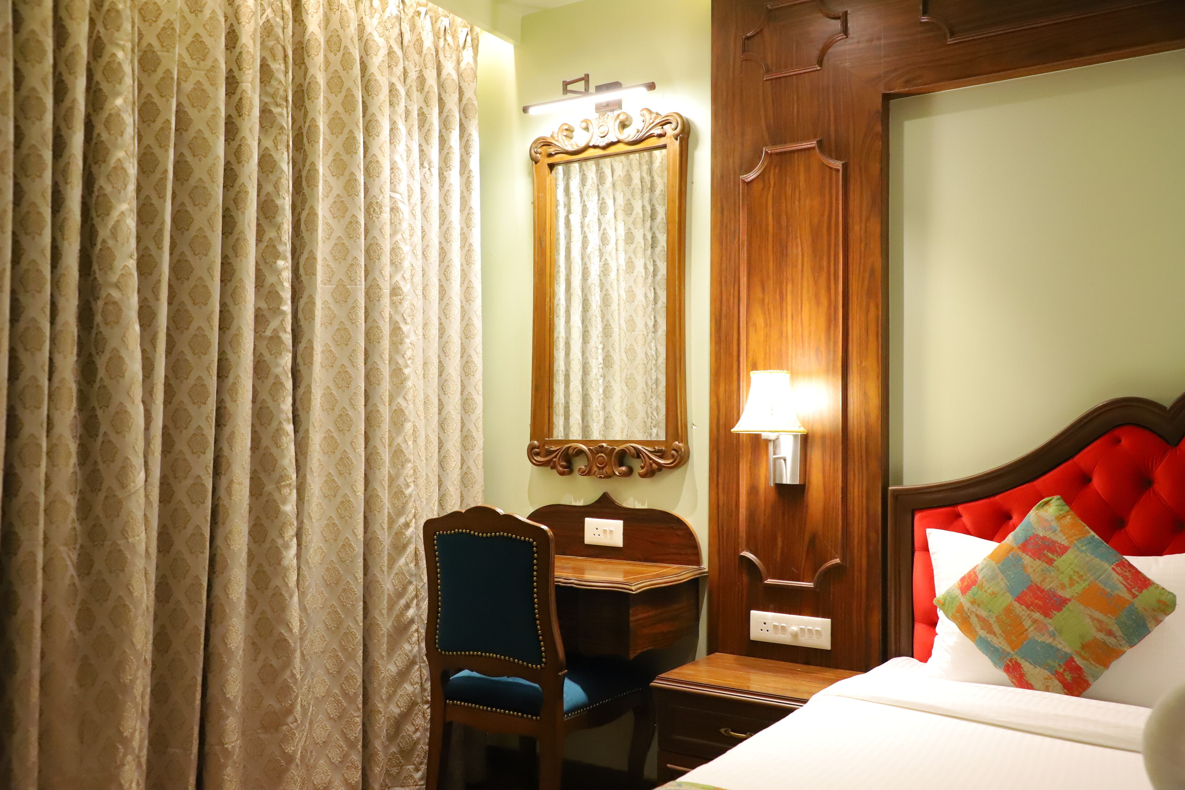 Una habitación de hotel con una cama, un escritorio de madera, una silla, un espejo y una cortina.