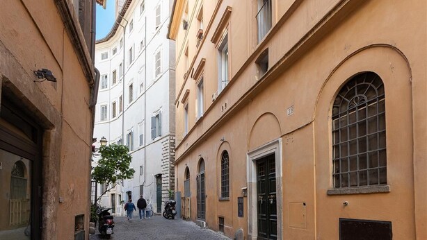 A narrow street with buildings on either side, featuring arched windows and doors, and a cobblestone path. - Navona Modern apartment (Rome)