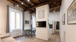 A spacious living area with a large window, a flat-screen TV mounted on the wall, a dining table, and a sofa. - Navona Modern apartment (Rome)