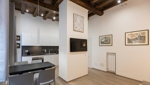 A modern kitchen with white cabinets, a black countertop, and a dining area with two chairs. There are framed artworks on the walls and a television mounted above the counter. - Navona Modern apartment (Rome)