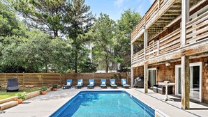 Une piscine rectangulaire dotée d’une terrasse en bois, entourée de chaises longues et de plantes en pot.