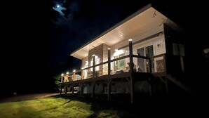 A modern house with a balcony, stone facade, and a well-lit interior.