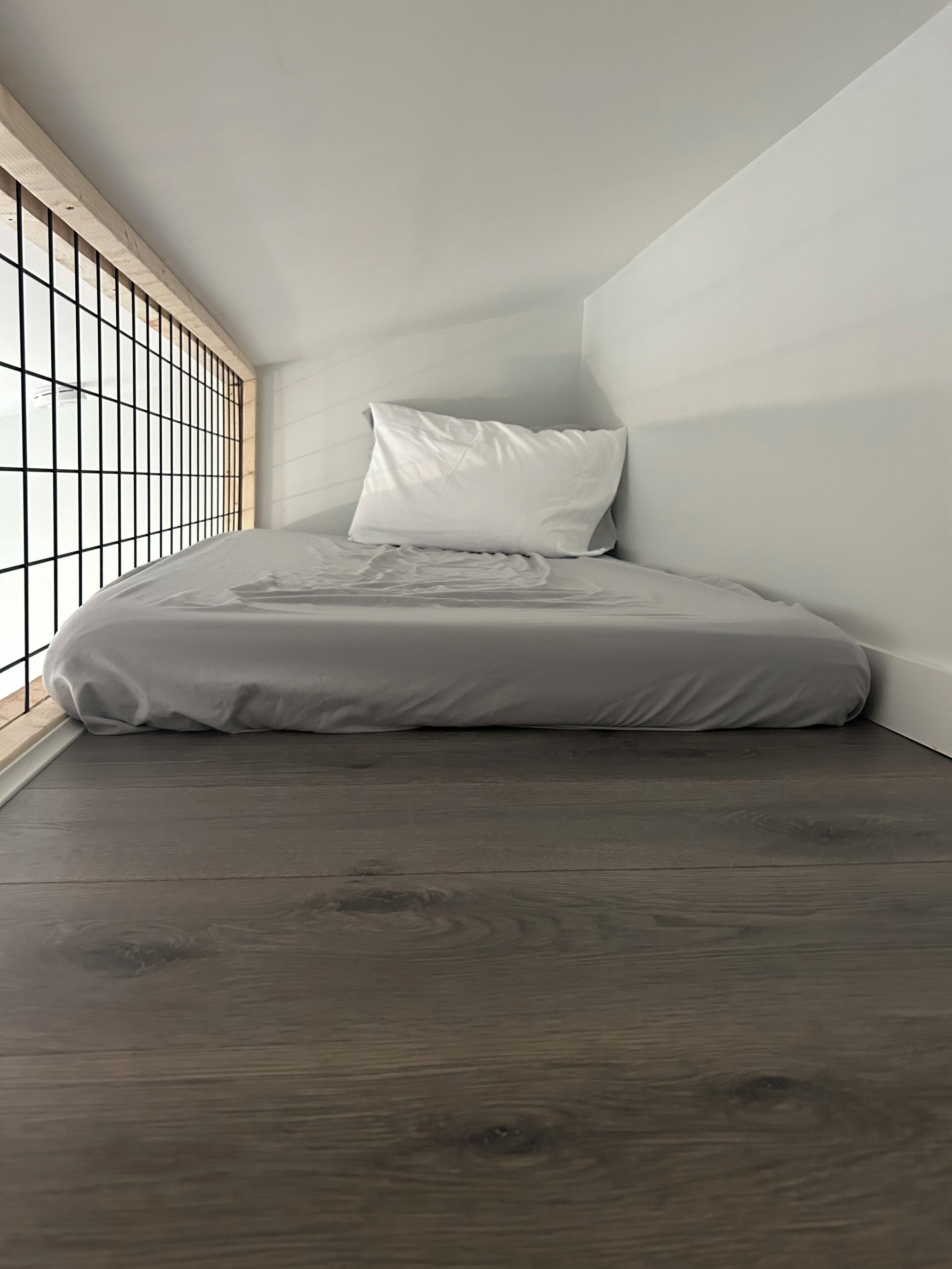 Ein kleines, modernes Schlafzimmer mit einem Bett, einem Fenster mit Gitterstruktur und Holzboden.